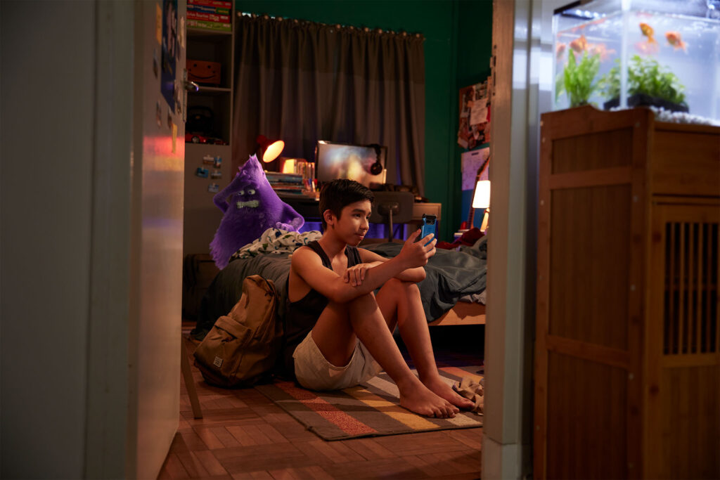 purple creature stressed in background of boy's bedroom who is on his phone